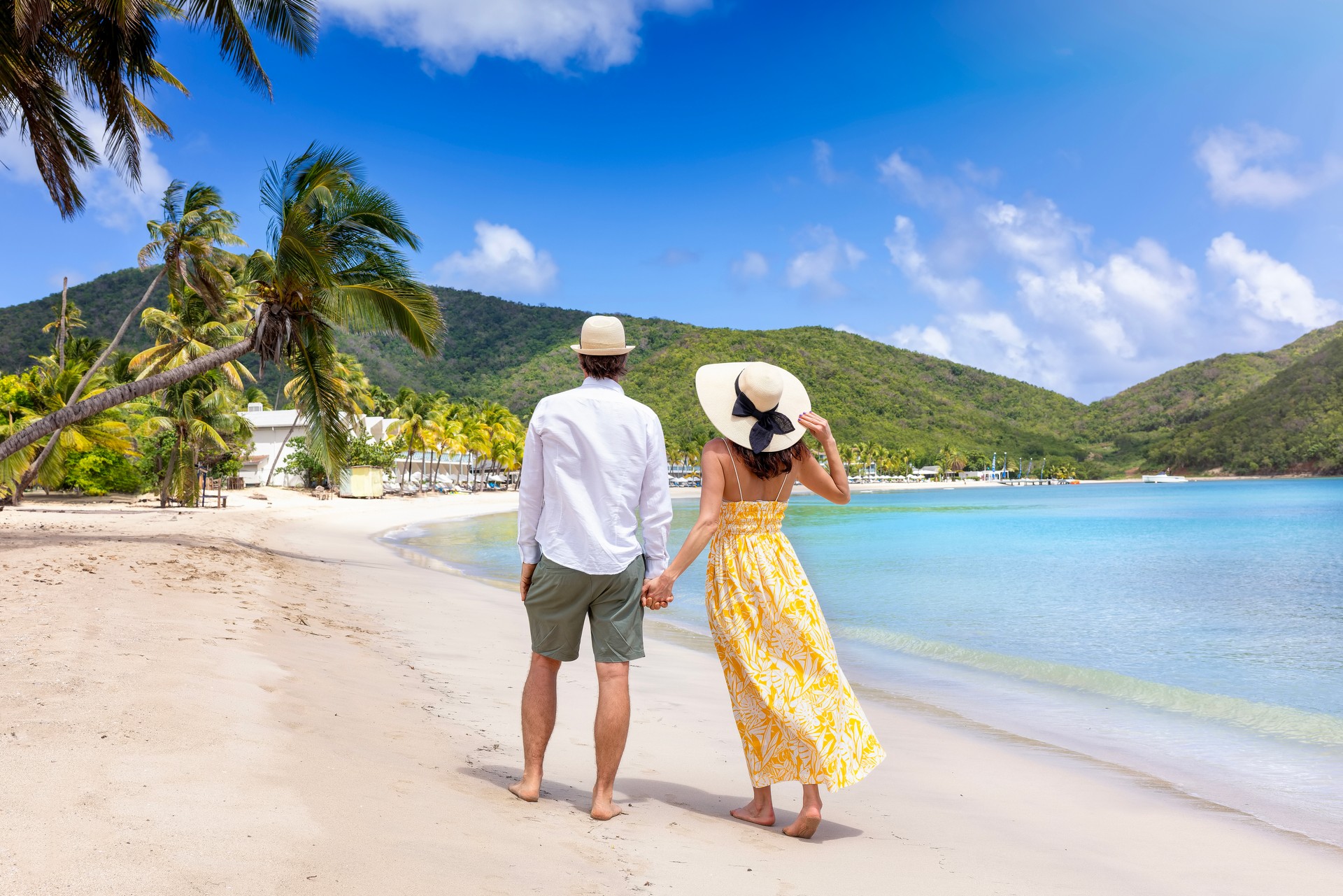 Happy holiday couple with sunhats walks down a tropical beach