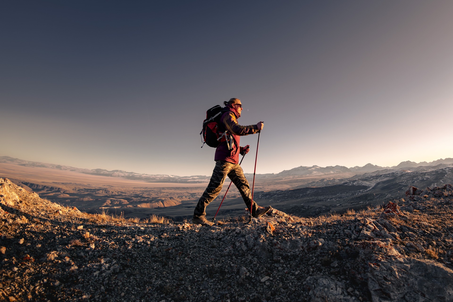 Man with backpack walks in sunset mountains